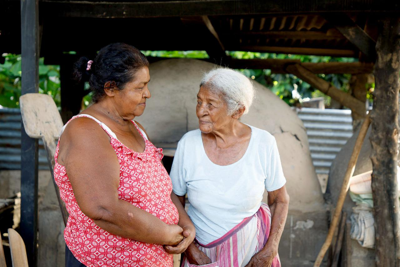 Dos mujeres de edad avanzada dándose la mano con una sonrisa. Una es mayor que la otra en la Zona Azul de Costa Rica