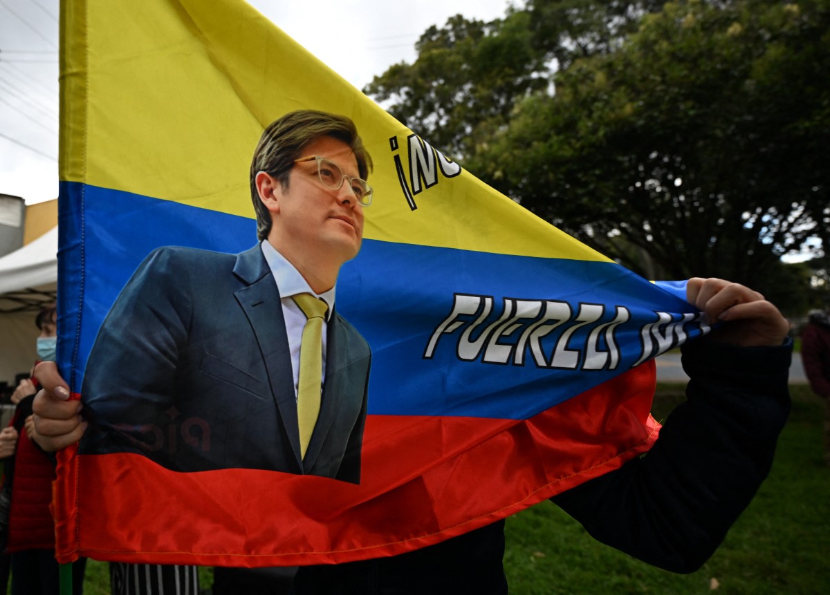 Una mujer sostiene una bandera colombiana con la imagen del candidato presidencial colombiano Miguel Uribe durante una misa por su salud en Bogotá el 21 de junio de 2025. El 19 de junio, las autoridades colombianas detuvieron a un cuarto sospechoso presuntamente implicado en el atentado contra el senador y candidato presidencial Miguel Uribe, que sigue hospitalizado en estado crítico, según informó la fiscalía. El senador, de 39 años, recibió tres disparos el 7 de junio, dos de ellos en la cabeza, durante un mitin político en un parque de Bogotá.