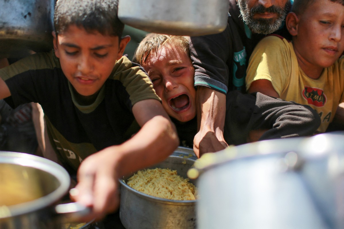 La gente intenta conseguir arroz en un comedor social que ofrece comida gratuita en el oeste de la ciudad de Gaza, el 28 de agosto de 2025, mientras continúa la guerra entre Israel y el movimiento militante Hamás. La ONU declaró la hambruna en la provincia de Gaza la semana pasada, culpando a Israel de la